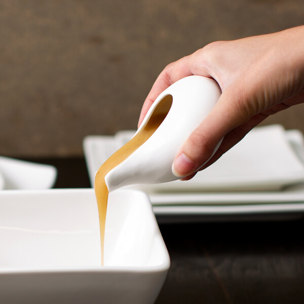 A person pouring brown gravy into a white bowl using a 10 Strawberry Street Whittier gravy tid bit.