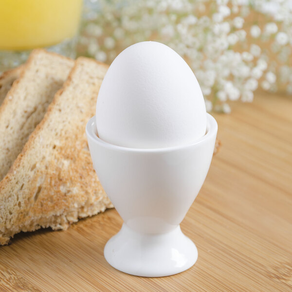 A white egg in a 10 Strawberry Street Whittier porcelain egg cup next to toast and juice.