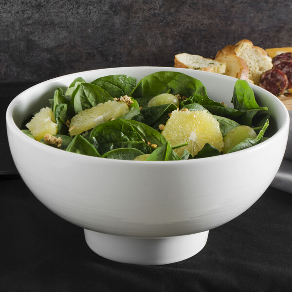 A white ribbed porcelain bowl filled with spinach and orange slices on a table.