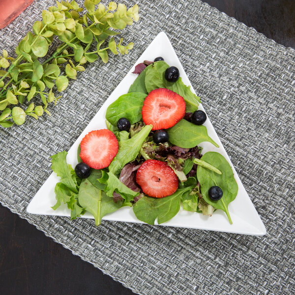 A white triangle porcelain plate with a salad of strawberries and blueberries.