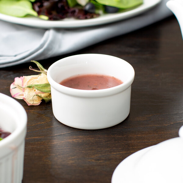 A white porcelain 10 Strawberry Street Whittier rim cup on a table with a bowl of red sauce.