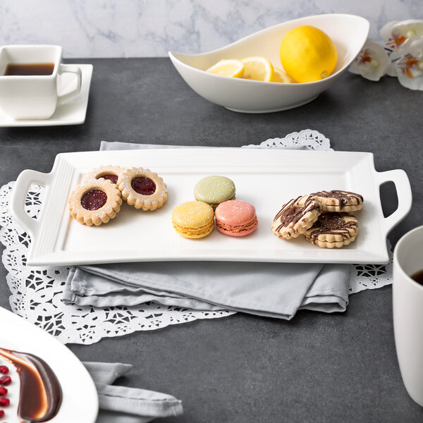 A white rectangular porcelain platter with cookies and a lemon on a table.
