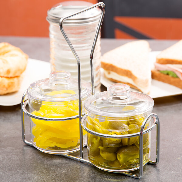 A Thunder Group wire condiment holder with glass jars of yellow mustard and green peppers.