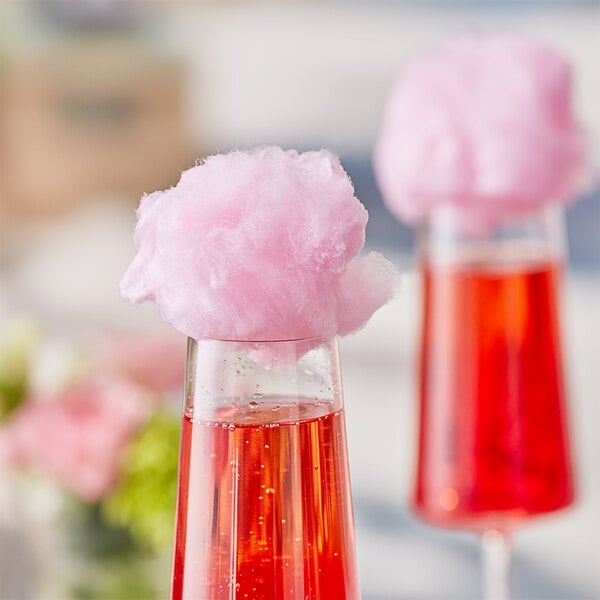 A close-up of a glass with pink liquid and a pink cotton candy on top.