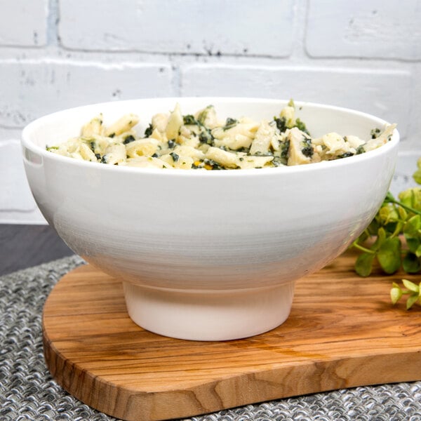 A white 10 Strawberry Street Whittier ribbed bowl filled with pasta on a wood surface.