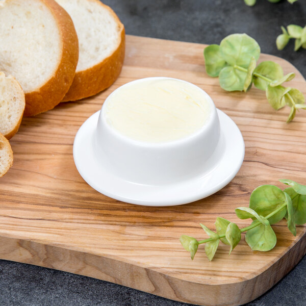 A white bowl of butter on a wooden board next to slices of bread.