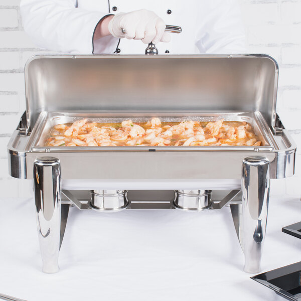 A person using a Vollrath stainless steel roll top chafer to serve food on a buffet table.