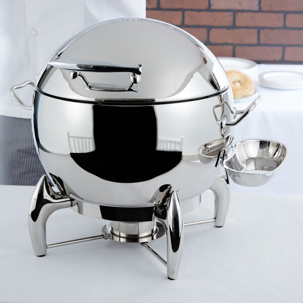 A Vollrath stainless steel chafing dish with a silver lid on a table.