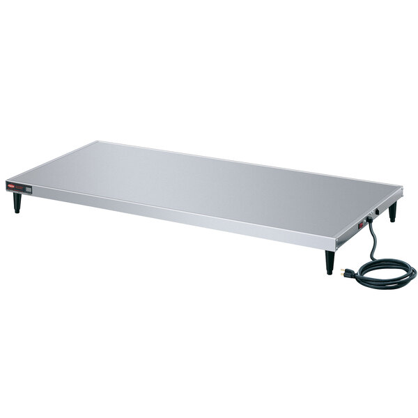 A white rectangular stainless steel Hatco heated shelf on a rectangular silver table with a black power cord.