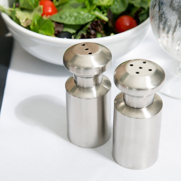 An American Metalcraft stainless steel salt and pepper shaker set on a table with a bowl of salad.