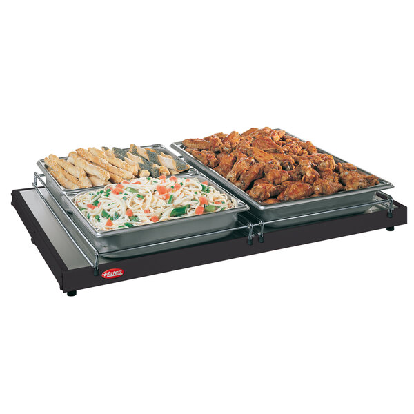 A Hatco portable heated shelf with trays of pasta, vegetables, and chicken wings on a table.