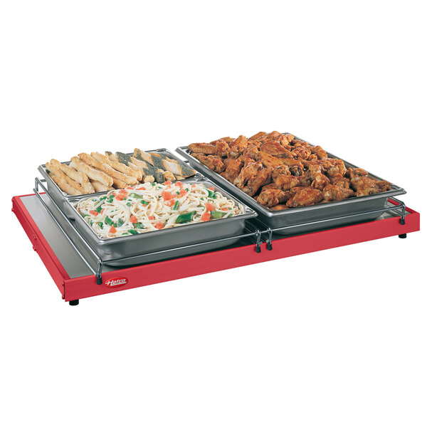 A Hatco red portable heated shelf with trays of food on a table.