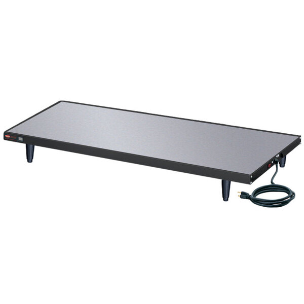 A rectangular black and silver Hatco heated shelf warmer with a cord on a table.