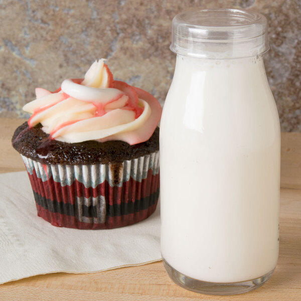 A cupcake with frosting on top on a wooden table next to an American Metalcraft Glass Milk Bottle filled with milk.