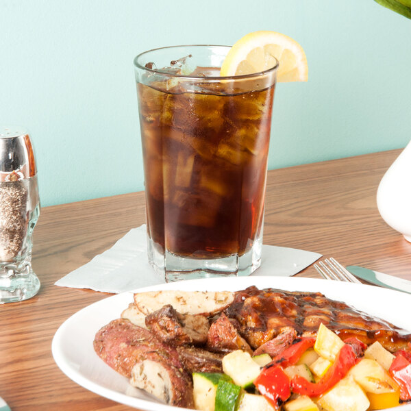 A plate of food and a Libbey Inverness beverage glass filled with brown liquid and ice on a table.