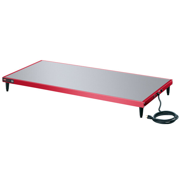 A red and grey rectangular Hatco heated shelf on a table with a black cord.