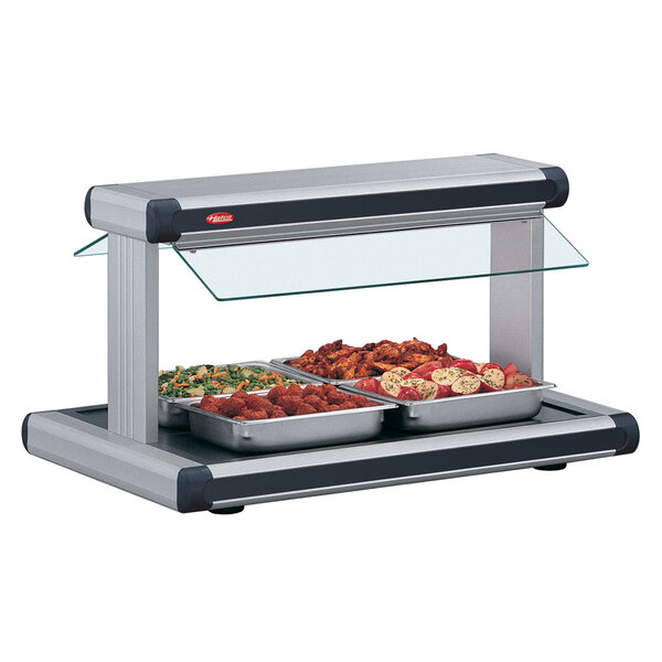 A Hatco buffet warmer with food on buffet trays under a glass counter top.