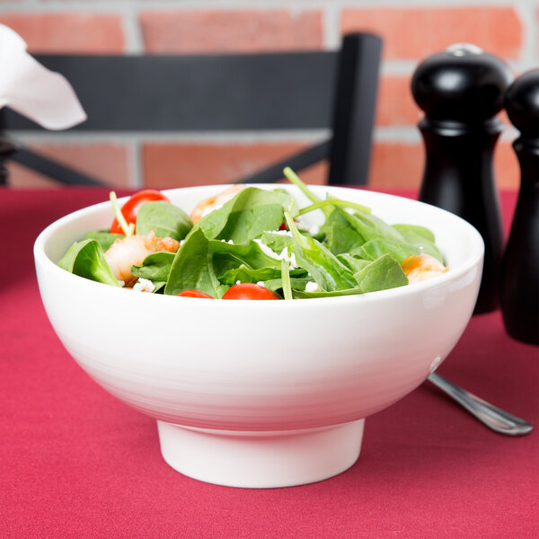 An American Metalcraft porcelain footed bowl filled with salad on a table.
