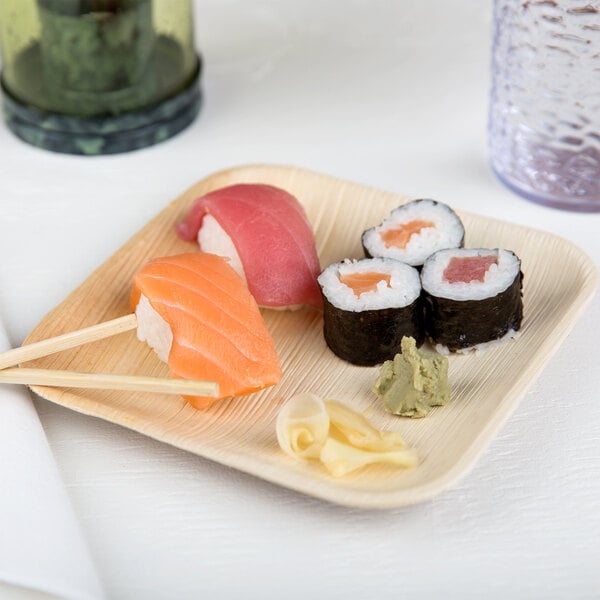 A square palm leaf plate with sushi and chopsticks.