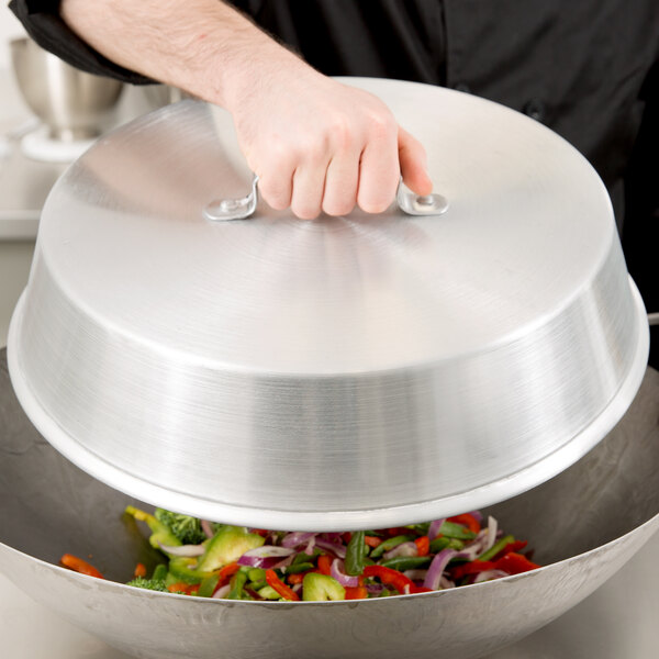 A person using a Town aluminum wok cover to cover a bowl of food.