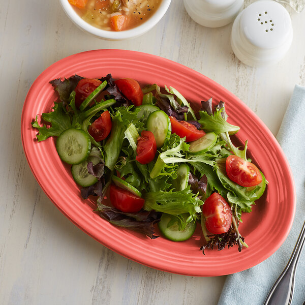 A Tuxton Cinnebar oval china platter with salad, tomatoes, cucumbers, and lettuce.