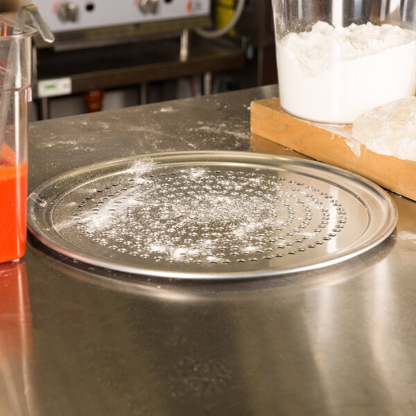 An American Metalcraft Super Perforated Heavy Weight Aluminum Wide Rim Pizza Pan on a counter with flour on it.