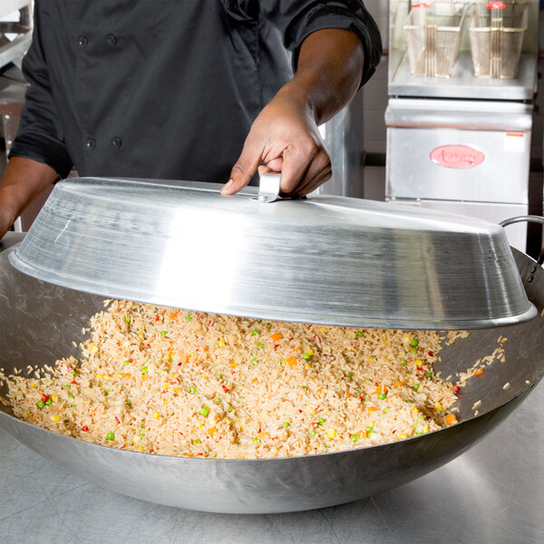 A chef using a Town aluminum wok cover to prepare a dish in a large wok.