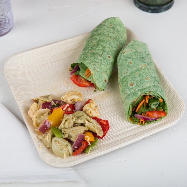 A Eco-gecko palm leaf plate with wraps and a salad on it on a white table.