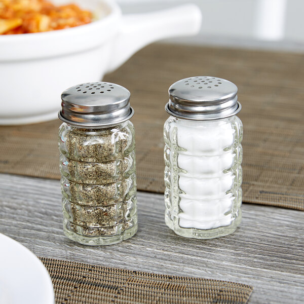 Two Tablecraft Nostalgia glass salt and pepper shakers with stainless steel tops on a table.