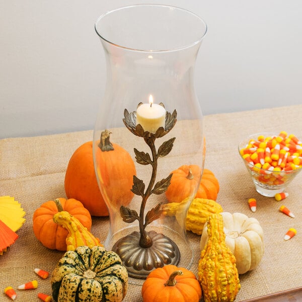 A Libbey glass hurricane shade with a candle inside on a table with pumpkins and candy corn.
