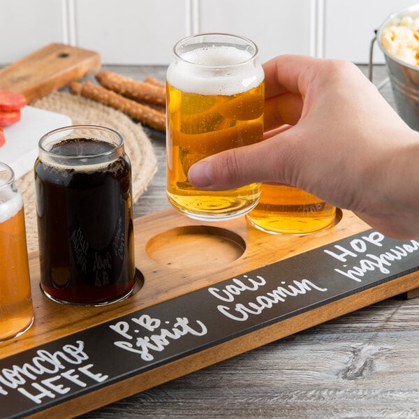 A person holding a Cal-Mil Madera natural flight tray with beer glasses filled with beer.