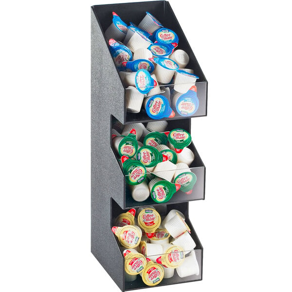 A Cal-Mil black three tier condiment display with clear bins holding coffee creamer, lids, and cups.
