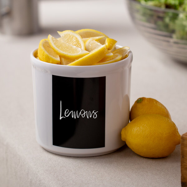 A white Cal-Mil melamine crock with a blackboard label holding lemons and limes.