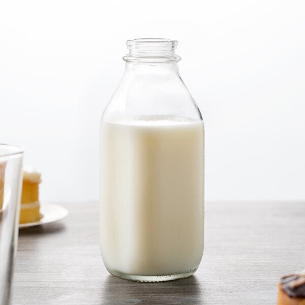 A Libbey glass bottle of milk on a table next to a glass of milk.