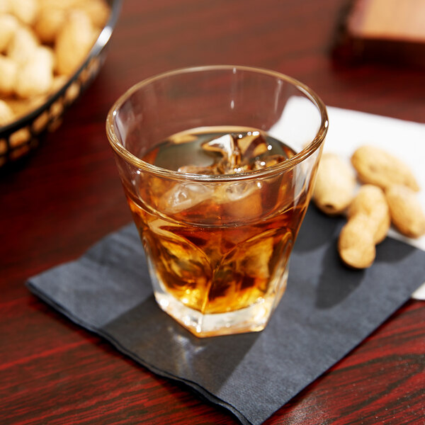 A Libbey Gibraltar twist rocks glass of amber liquid with ice on a table with peanuts on a napkin.