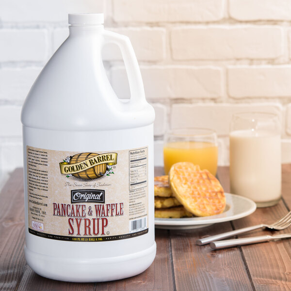 A white jug of Golden Barrel Pancake and Waffle Syrup next to a plate of waffles.
