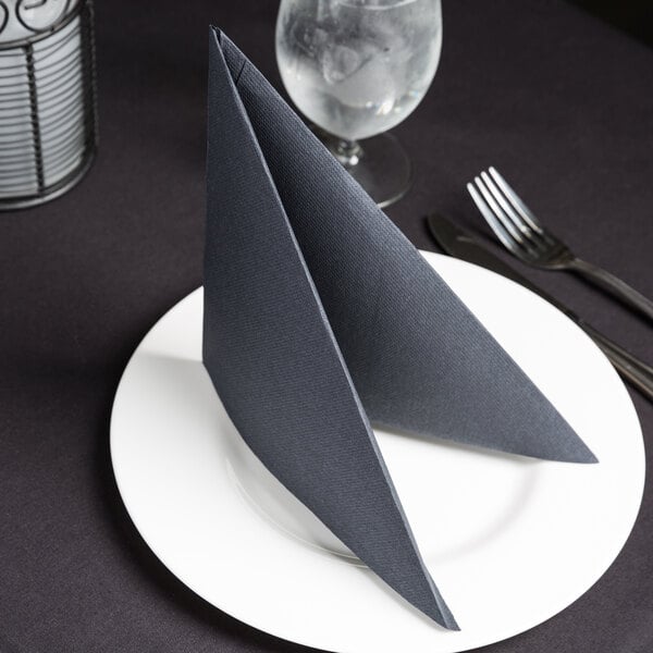 A folded black Hoffmaster FashnPoint dinner napkin on a white plate with silverware.