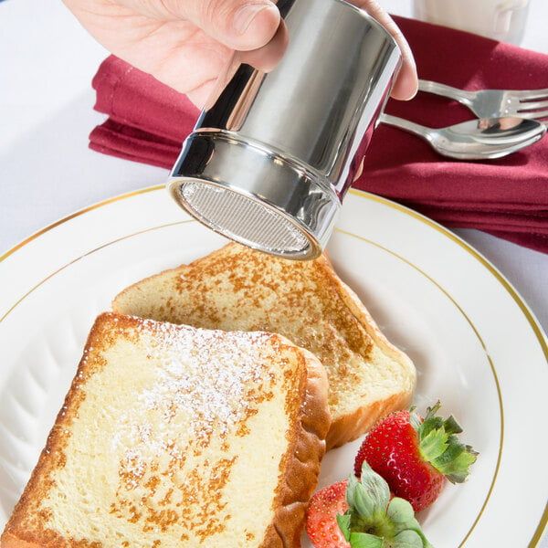 A person using an Ateco powdered sugar shaker to pour powdered sugar onto a piece of toast.