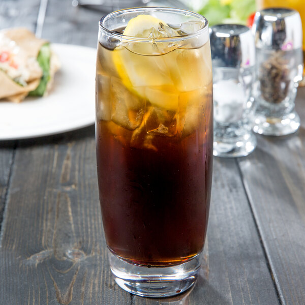 An Arcoroc customizable cooler glass of iced tea with ice and lemon on a table.