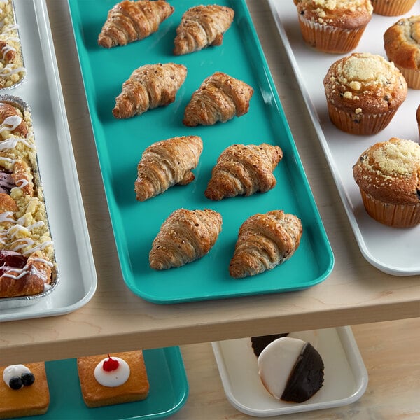 A green Cambro market tray holding pastries and muffins on a bakery display counter.