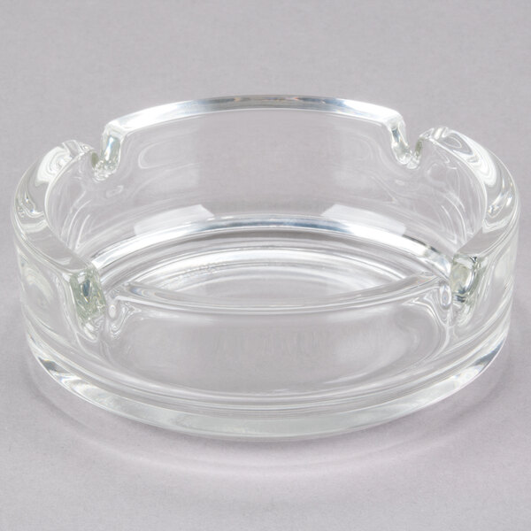 A clear glass Arcoroc ashtray with a small hole in the center.