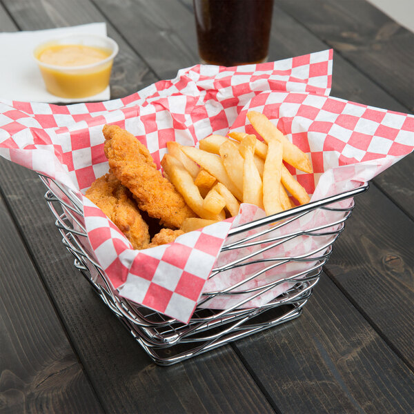 An American Metalcraft chrome square birdnest basket holding chicken and french fries on a table in a food truck.