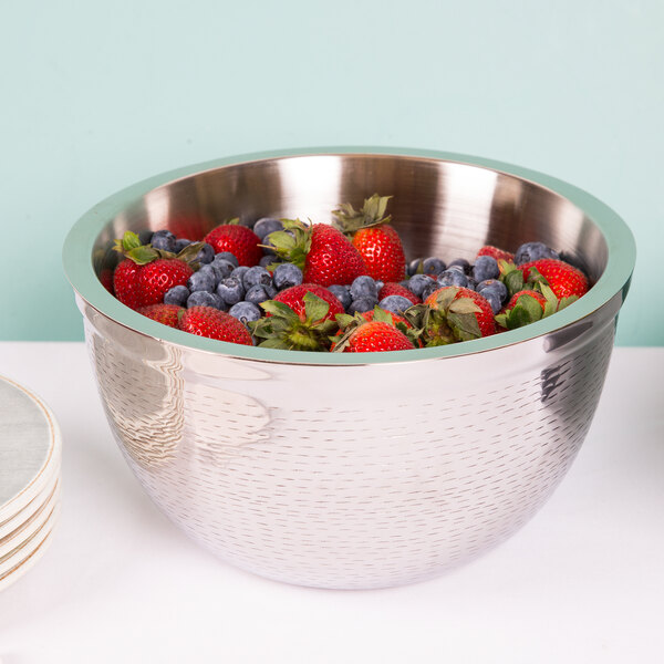 A Tablecraft Remington stainless steel bowl filled with strawberries and blueberries on a table with a stack of plates.