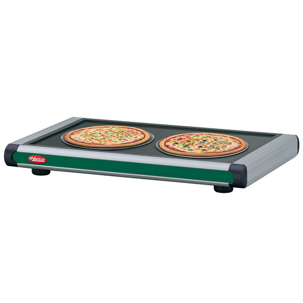 A Hatco Glo-Ray heated shelf with pizza pans holding two pizzas on a table.
