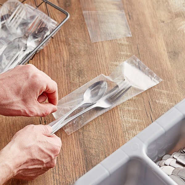 A hand putting a spoon in a plastic silverware bag.