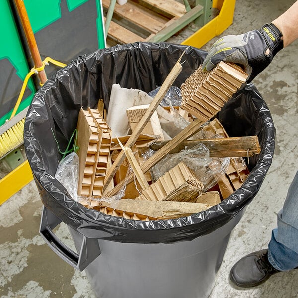A person holding a wood piece in a trash can.