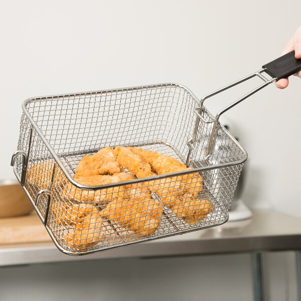 A hand holding an Avantco fryer basket filled with fried chicken.