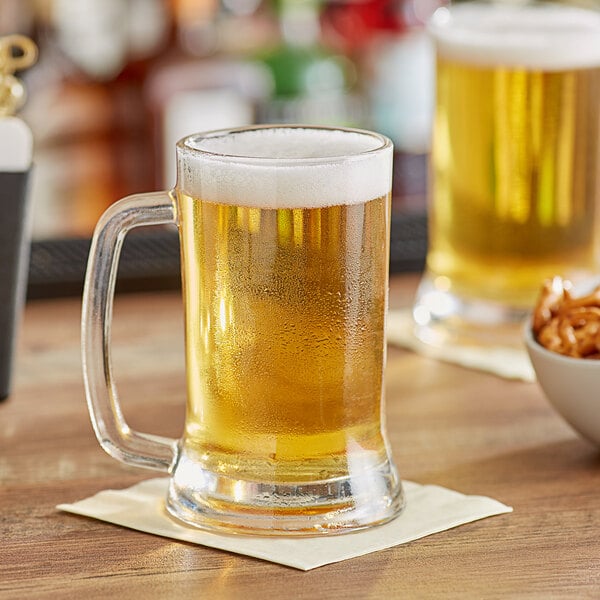 Two Acopa beer mugs filled with beer on a table with snacks.