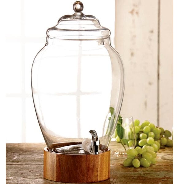 An American Atelier glass beverage dispenser with a wood base on a counter.