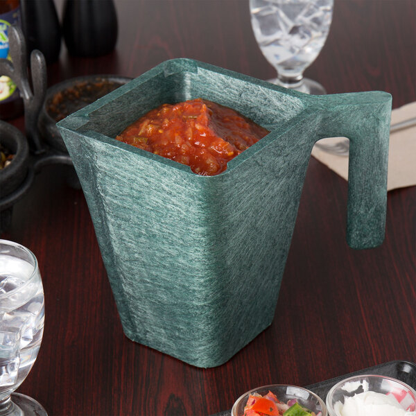 A green HS Inc. jalapeno pitcher filled with red salsa on a table.